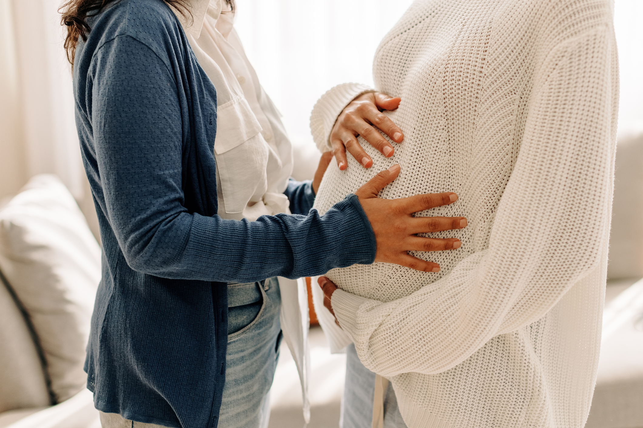 Unrecognizable young woman touching her surrogate’s pregnant bel